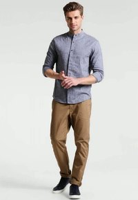 Camisa de linho azul claro, de botões, com colarinho levantado e mangas arregaçadas; combinada com chinos bege e sapatilhas azuis marinhas.