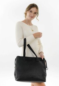 Sac en cuir noir à texture granuleuse, avec deux poignées solides et une fermeture zippée. Accentué d'un petit pendentif sur la tirette de la fermeture.