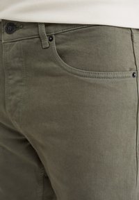 Lähellä näkyvän oliivinvihreän housun taskun, jossa näkyy saumat, vyölenkki ja nappi, jossa on "Blue Ridge" -brändäys vyötäröllä.