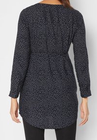 Marineblaue Langarm-Tunika mit weißen Polka-Dots, ausgestattet mit einem gerafften Rücken, abgerundetem Saum und Knopfmanschetten. Aus weichem, leichtem Stoff.