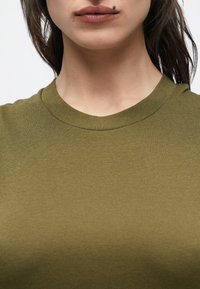 Camiseta de manga corta con canalé en verde oliva, con cuello redondo, textura suave y silueta ajustada.