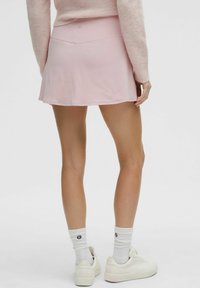 Roza atletska suknja s otvorenim krojem i glatkom teksturom, uparena s bijelim tenisicama i čarapama s logom.