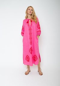 Różowa lniana sukienka z haftowanymi czerwonymi wzorami paisley, z długimi rękawami, dekoltem typu keyhole i bocznymi rozcięciami.