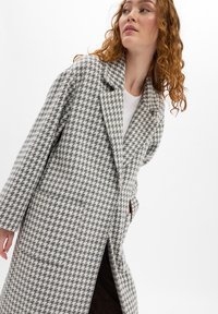 Grijze en witte houndstooth-gepatroniseerde jas met een ingesneden kraag, lange mouwen en zijzakken. Gemaakt van textiel met een structuur.