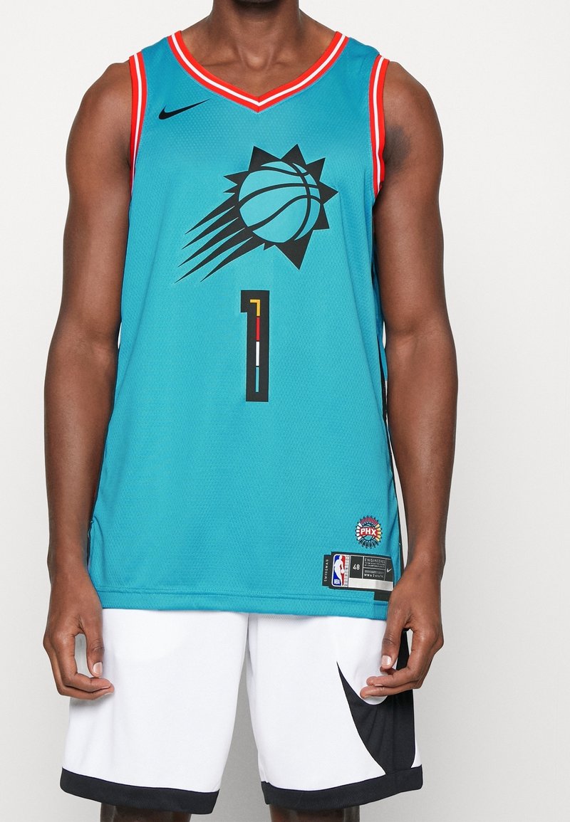 Homme portant un maillot de basket turquoise des Phoenix Suns avec le numéro un et un short blanc avec un motif noir, debout devant un fond uni.