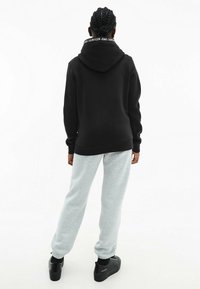 Felpa nera con colletto con logo, abbinata a pantaloni della tuta grigio chiaro e sneakers platform nere. Cuciture visibili e polsini a costine.