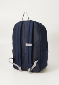 Granatowy plecak z padded, regulowanymi szarymi paskami, teksturowanym materiałem i naszywką z logo. Posiada uchwyt na górze oraz boczną siatkową kieszeń.