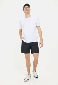 Witte T-shirt met korte mouwen, gecombineerd met donkerblauwe shorts en witte sneakers. Het T-shirt heeft een klassieke ronde hals en een ontspannen pasvorm.