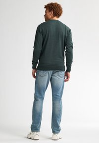 Donkergroene trui met lange mouwen en een ronde halslijn. Gepaard met lichtblauwe jeans en witte sportschoenen. Eenvoudig ontwerp, geen zichtbare patronen.