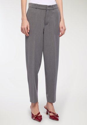 Donna che indossa pantaloni grigi a vita alta su misura abbinati a tacchi slingback rossi a punta con cinturini e fibbie.