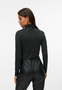 Mustretega mustakätise turtleneck-särk, millel on tekstuuriga kangas ja peen sära, koos kõrge vöökohtadega mustade kunstnahkpükstega.