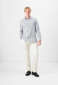 Camisa de cuadros gris con botones y un bolsillo en el pecho, combinada con pantalones cremosos y zapatos negros. La camisa tiene mangas largas y un collar.