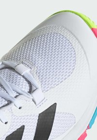White athletic shoe with a textured mesh upper, black accents, and a multicolored sole featuring pink, green, and blue details.