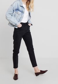 Jasnoniebieska kurtka dżinsowa, biała koszulka, czarne dżinsy z wysokim stanem i burgundowe mokasyny. Swobodny krój, klasyczny design i gładka tekstura.