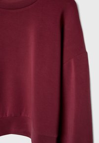 Sweat-shirt bordeaux à manches longues avec col et ourlet côtelés, présenté sur un fond gris clair.
