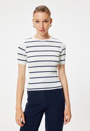 Top de punto de manga corta en blanco con rayas marinas. Presenta una textura acanalada y un escote redondo. Combinado con pantalones de un azul marino oscuro.