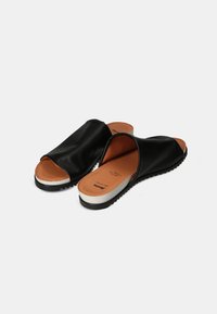 Sandales à glissière en cuir noir avec un bout ouvert, un haut incurvé et des semelles intérieures orange. Elles possèdent une semelle intermédiaire blanche et une semelle extérieure noire texturée.