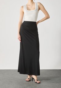 Zwarte maxi-jurk van gladde stof met een elastische tailleband, gecombineerd met een wit geribd tanktop met vierkante halslijn.