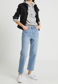 Czarna kurtka jeansowa z kołnierzem z futerka, szara bluza z kapturem z nadrukiem Boston, jasnoniebieskie proste jeansy i białe trampki.