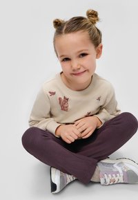 Beige sweatshirt met dierenprints, gecombineerd met geribde donkerpaarse leggings. Zilveren en pastel sneakers hebben gaas- en glinsteraccenten.