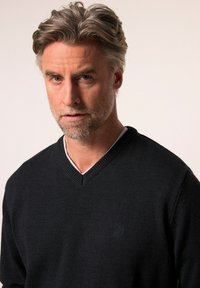 Dunkelblauer V-Ausschnitt-Pullover mit gestrickter Textur, versehen mit einem Logo auf der linken Brust. Der innere Kragen ist weiß und sorgt für einen Kontrast.