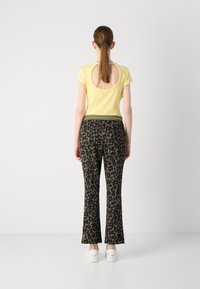Geel T-shirt met korte mouwen en een grote uitsnijding op de rug, gecombineerd met zwarte flared pants met een groen en beige luipaardprint.