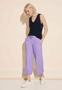 Granatowy bezrękawnik i jasnopurpurowe spodni cropped z troczkiem w talii. Całość uzupełniają białe sneakersy.