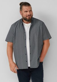 Korte mouwen, gestreept shirt in marineblauw en wit, met een button-down kraag en een ontspannen pasvorm, gedragen over een wit t-shirt.