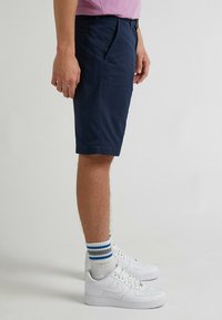 Pantaloni corti blu navy con una vestibilità su misura, realizzati in materiale leggero. Abbinati a sneakers bianche e calze sportive a righe.