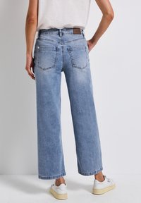 Jeans de pierna ancha en azul claro, fabricados en denim, con una cintura alta, cinco bolsillos y una parche de cuero marrón en la parte posterior de la cintura.