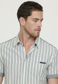 Chemise à manches courtes en tissu léger avec des rayures verticales bleues et blanches. Dotée d'une poche poitrine avec un logo "Lee Cooper".