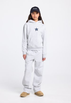Gray hoodie and sweatpants set with a star graphic, featuring a front pocket. A navy cap with “New York” text and tan footwear completes the outfit.