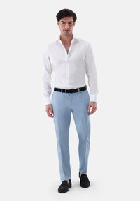 Weißes Hemd mit langen Ärmeln kombiniert mit hellblauen Hosen in Slim Fit. Das Outfit wird mit schwarzen Slippern vervollständigt.