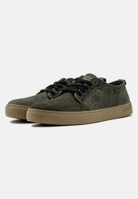 Cipő: olajzöld velúr alacsony szárú sneaker, kerek orral, fekete fűzővel és bézs gumitalppal, amelynek varrási részletei és logó kiemelései vannak.