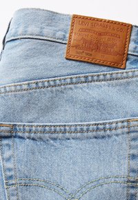 Jean en denim bleu clair avec un patch en cuir marron Levi Strauss & Co. affichant la marque et les détails de la taille au-dessus de la poche arrière.