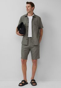 Casual outfit met een grijze linnen overhemd met korte mouwen, bijpassende shorts, een wit T-shirt, zwarte sandalen en een zwarte tas.