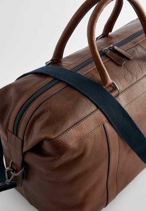 Hnědá kožená cestovní taška s texturovaným povrchem, vrchními úchyty a modrým nastavitelným popruhem. Disponuje zipovým uzávěrem a kontrastním prošíváním.