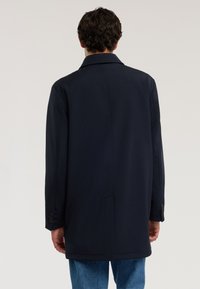 Marineblauer Mantel, maßgeschneidertes Design mit geradem Rücken, langen Ärmeln und geknöpften Manschetten. Glatte Textur und minimale Nähdetails.