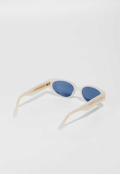 Cat-eye sunglasses with clear frames, blue tinted lenses, and light-colored arms. Features gold hardware details on the temple.