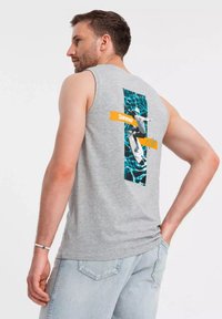 Šedé tílko bez rukávů s barevným grafickým designem a textem "Léto". Vyrobeno z měkké látky s jemnou melírovanou strukturou.