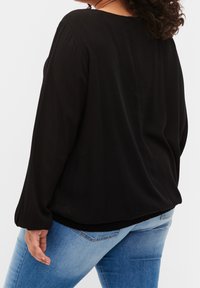 Blouse noire à manches longues à coupe décontractée, avec un col rond et un tissu doux et texturé. Associée à un jean en denim bleu clair.