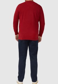 Rode gebreide trui met lange mouwen, geribbelde manchetten en een ronde halslijn, gecombineerd met donkerblauwe jeans en witte sneakers.