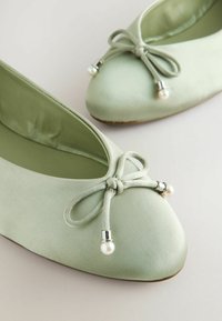 Bailarinas de satén verde menta con punta redonda, detalle de moño de tela con herrajes plateados y acentos de perlas. Textura suave, diseño minimalista.