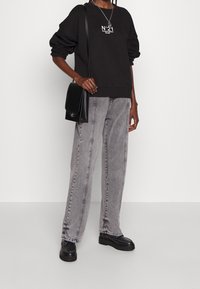 Black sweatshirt with white "N°21" text, paired with gray wide-leg jeans. Features black leather crossbody bag and black platform loafers.