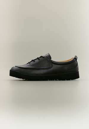 Chaussure basse en cuir noir avec panneau avant texturé, design à lacets, languette au talon et semelle épaisse en caoutchouc isolée sur fond gris.