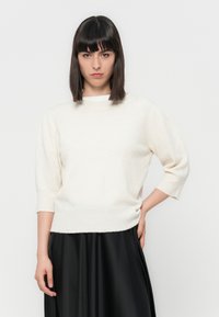 Pull en maille écru avec des manches trois-quarts et un col rond, doté d'une texture douce et d'un ourlet en côtes, associé à une jupe en satin noire.