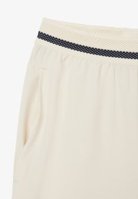 Pantalones cortos color crema con una cinturilla elástica texturizada que presenta acentos de color azul oscuro. Incluye bolsillos laterales y un corte relajado.