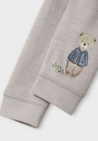 Grått tyg med manschetter som har en liten illustration av en björn i blå jacka och bruna byxor bredvid ett blått leksakståg.