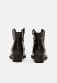 Botas de cuero negras hasta el tobillo con un bajo tacón de madera, que cuentan con un cierre de cremallera y un sutil estampado en relieve en la parte posterior.
