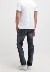 Mörkblå denimjeans med slim fit, urtvättade områden och signatur bakfickor. I kombination med en enkel vit t-shirt i bomull och vita sneakers.
